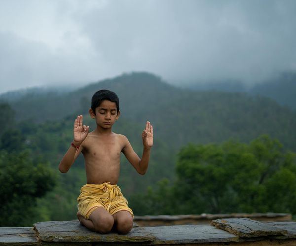 Person meditating peacefully outdoors with a serene landscape background.